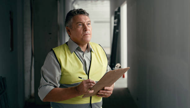 Man, architect and inspection with clipboard for maintenance check, safety or repair in construction on site. Serious male engineer in architecture, building or contracting writing industrial report stock photo