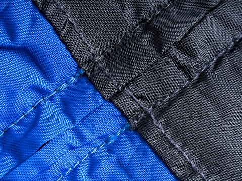 Nylon rain repellent storm jacket with zipper flap as an abstract textile. Blue and black fabric with stitching details and room for copy.