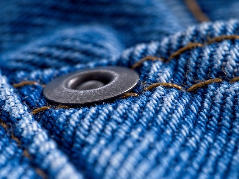 Macro abstract of blue jeans denim with brass rivet strengthening the material. Denim fabric focused on rivet with shallow depth of field. Highly detailed with room for copy space.