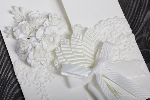 Homemade greeting card in white. With decorative elements. Ribbons, flowers and leaves are attached to cardboard. Close-up.