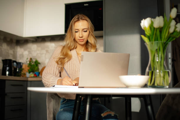 istock Use of modern technologies. Charming blonde is working, studying, online on laptop while in your modern kitchen. 1438435143