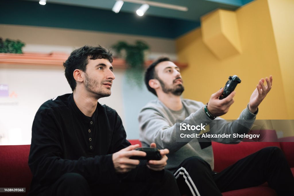 Male portrait of two beard men who playing video game on digital console indoors. People holding gamepad in the hands. Xbox and Playstation concept photography. Playing Stock Photo
