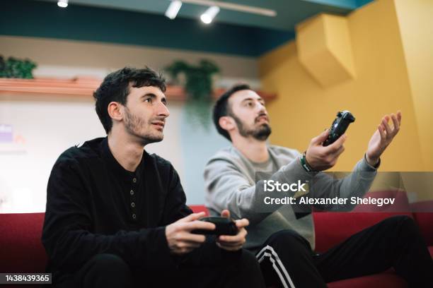 Male Portrait Of Two Beard Men Who Playing Video Game On Digital Console Indoors People Holding Gamepad In The Hands Xbox And Playstation Concept Photography Stock Photo - Download Image Now