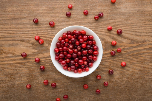 Full white bowl with fresh red cranberries on dark brown wooden table background. Eating healthy berries. Closeup. Top down view.