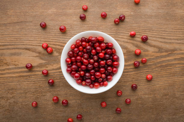 Full white bowl with fresh red cranberries on dark brown wooden table background. Eating healthy berries. Closeup. Top down view. stock photo