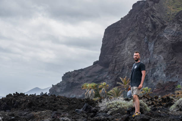 istock Caucasian young man standing in the black rocks in a cloudy day 1438440930