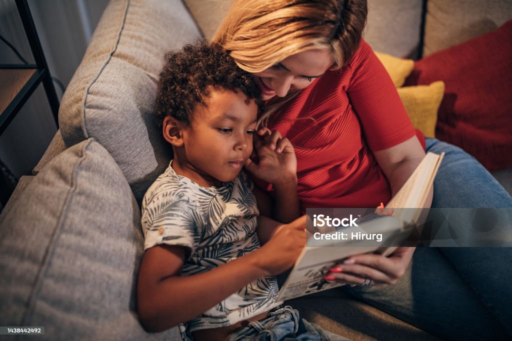 Mother and son reading stories Two people, young mother and her son reading stories together in the living room at home. Reading Stock Photo