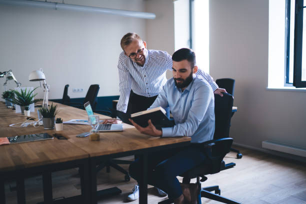 istock Smiling male employees sitting at table together reading report and analyzing accountings for startup enjoying cooperation, professional men designers talking to each other and having discussion 1438443241