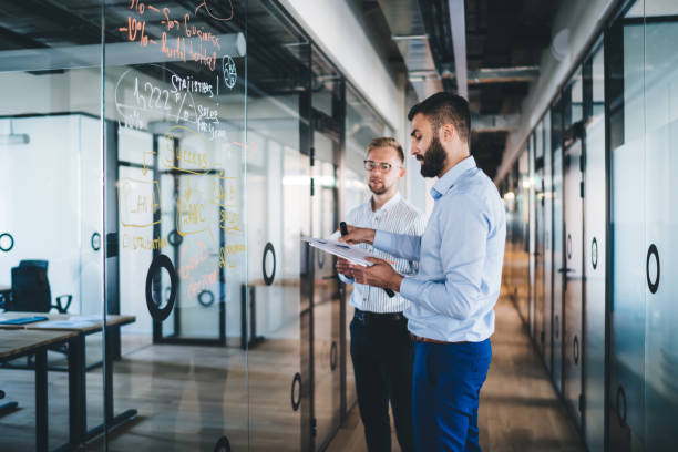 istock Smart casual men colleagues having productive cooperation on job share ideas during productive conversation in modern workspace with glass board, confident male marketers discussing analytic report 1438443826
