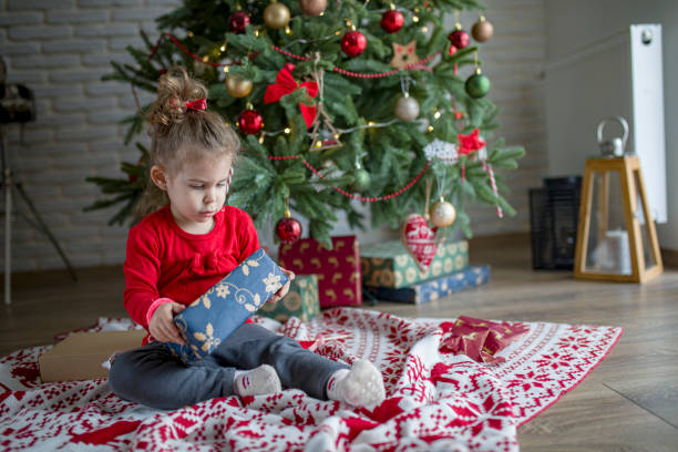 istock Cute little toddler opening present near Christmas tree 1438443858