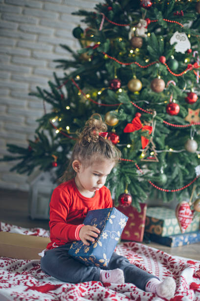 istock Cute little toddler opening present near Christmas tree 1438444211
