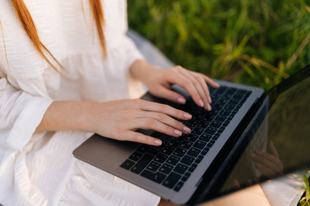 istock High-angle view of close-up hands unrecognizable female freelancer working typing on laptop computer sitting on beautiful field with green grass. 1438444331