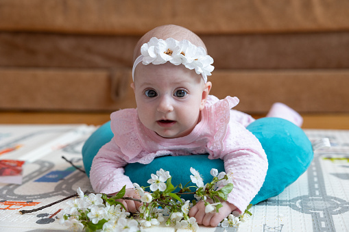 The baby lies on the floor and holds a branch of cherry blossoms. The baby is five months old.