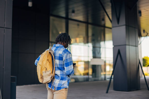 istock Back view of business man in plaid shirt with backpack going to work and using mobile phone 1438445770