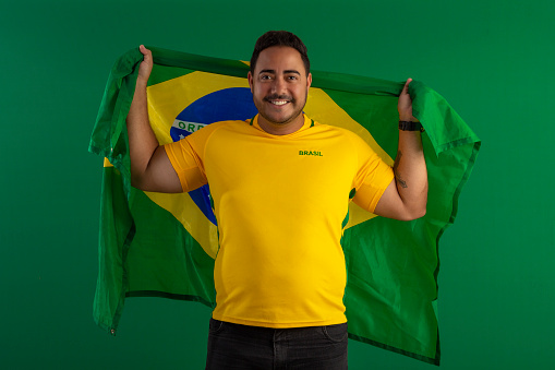 Brazilian man, soccer fan, with the shirt of the Brazilian team or with the flag of Brazil in studio photo with facial expressions