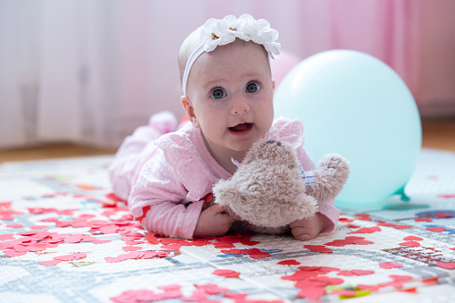 The baby lies on a soft children's play mat. The baby is holding a teddy bear in her hands. The baby is five months old.