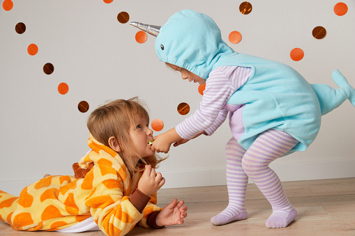 Cute little girls in giraffe and narwhal costume play at home. Halloween party celebration concept