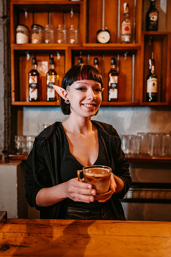 Young female barista wearing elf ears and serving a cup of coffee.