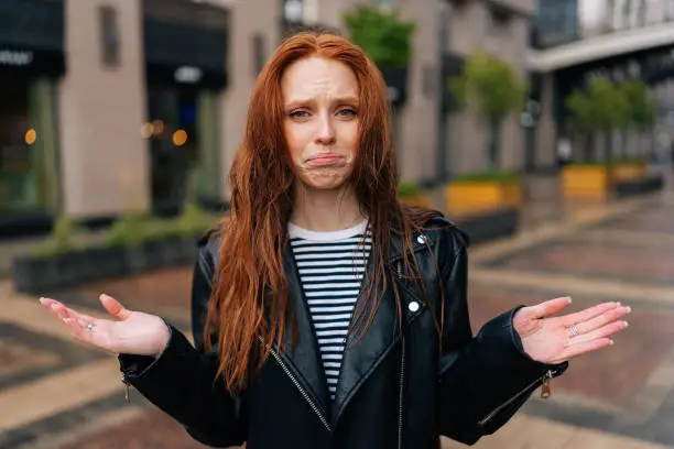 Portrait of distraught young woman with long red-hair standing with wet, disheveled hair after being caught in cold autumn rain, crying looking at camera. Concept of female lifestyle at autumn season.