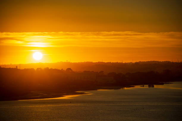 Amazing orange sunset with clouds forming a barrier for the light, a silhouette of the city and great reflection of the light at the water.