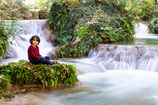 hiking boy taking a break in front of waterfall view. Taken in the autumn season. Taken with a full-frame camera using the long exposure technique.