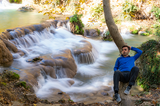 hiking man taking a break in front of waterfall view. Taken in the autumn season. Taken with a full-frame camera using the long exposure technique.