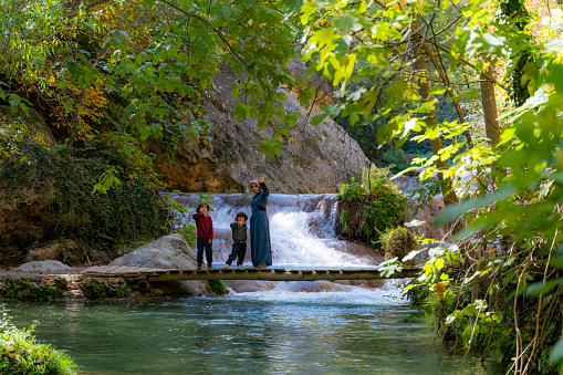 Boys walking with their mothers by the stream in the view of the waterfall. Taken in the autumn season. Taken with a full-frame camera using the long exposure technique.