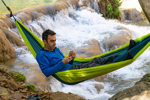 man stretching in hammock at waterfall view. Taken in the autumn season. Taken with a full-frame camera using the long exposure technique.