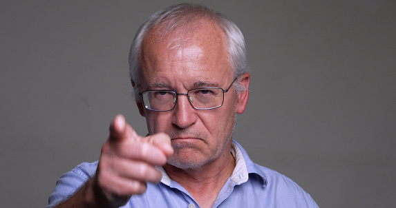 Serious, angry man, pointing at you on gray background