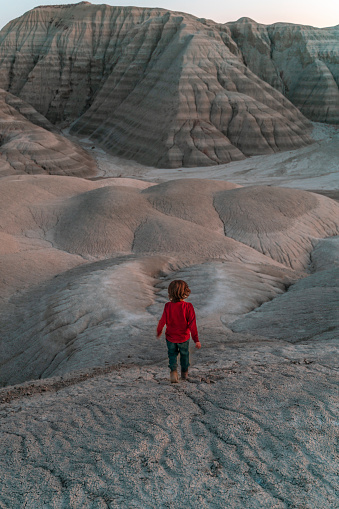 boy walking on desert land. colorful hills consisting of limestone, gypsum, marl and clay soils are visible. Taken from a high angle with a full frame camera.