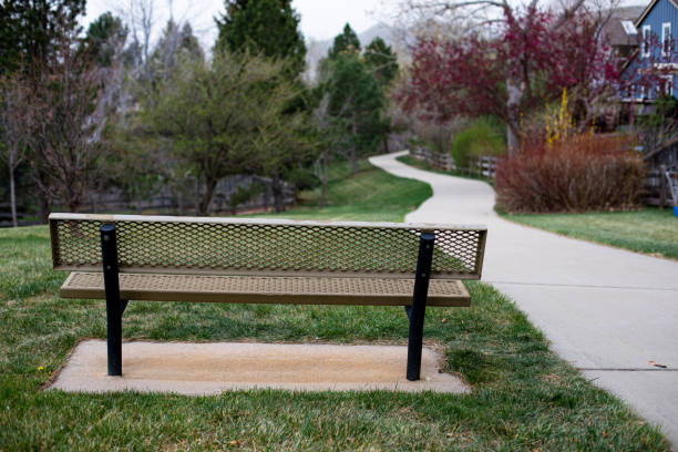 istock Park bench overlooking greenbelt in spring with blurred concrete path leading into trees with blurred houses on side 1438462157