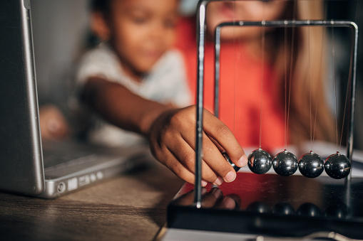 Two people, young mother and her son together at home. Boy is playing with newton's cradle.