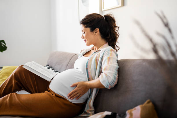 istock Young pregnant woman at home reading a book 1438464276