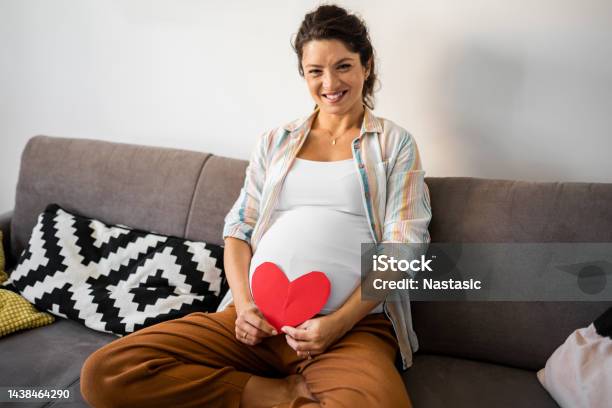 Smiling Pregnant Woman Holds Heart Shape On Pregnant Belly Looking At Camera Stock Photo - Download Image Now