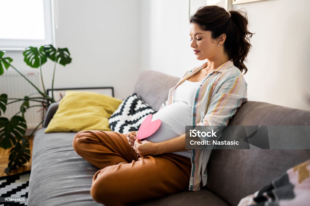 Smiling pregnant woman holds heart shape on pregnant belly A pregnant woman holds an heart shape Pregnant Stock Photo