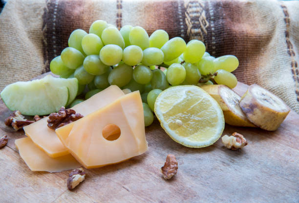 Food composition  from cheese and fruts and walnuts:  Emmental cheese,  light  grapes, cut Lemon, pieces of banana, pieces of green apple, walnuts  on wooden  desk