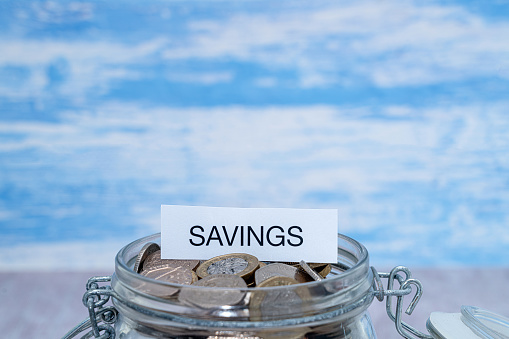 A paper label with the word Savings on top of a glass jar of coins