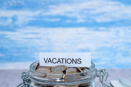 A paper label with the word Vacations on top of a jar of coins