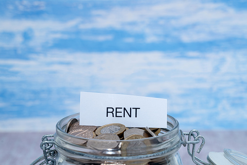 A paper label with the word Rent on top of a glass jar of coins