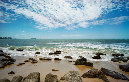 Looking north from Alexandra Headland beach, a coastal part of Maroochydore,Sunshine Coast, Queensland, Australia. Rocky foreshore with waves breaking and cloudy blue sky.