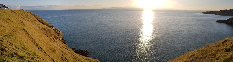 A panoramic high angle shot of the light of the sun over ocean surrounded by hills