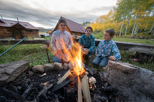 Three Young Farm Boys Enjoying a Campfire in the Forest Behind Their Homestead in the Mountains of Colorado Near Telluride