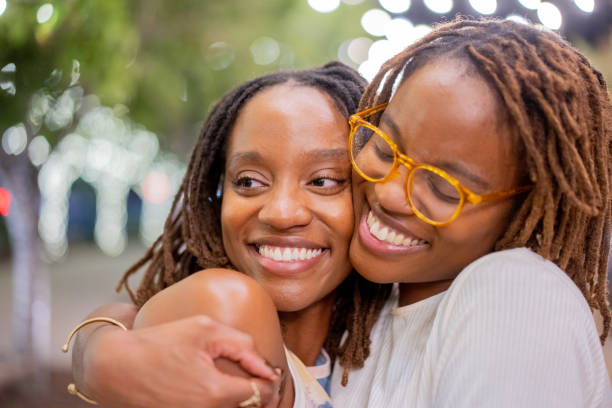 Two Happy African-American Twin Sisters in Their Twenties Embracing Each Other Lovingly with Happy Smiles stock photo