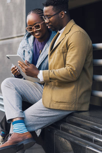 istock Couple of friends sitting on a bench, using a digital tablet 1438484979
