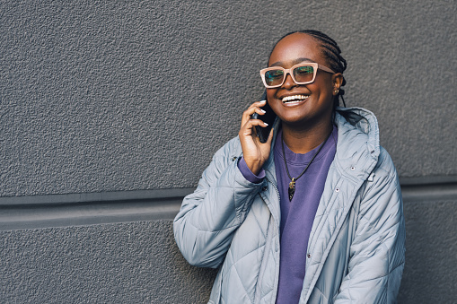 Beautiful young black woman with sunglasses using her cell phone. Young black woman smiling while having a conversation over the phone.