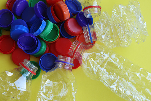 Bottle caps and plastic bottles on the yellow background with copy space