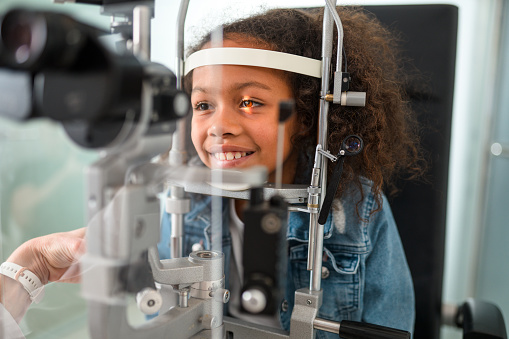 Adorable smiling black girl having her eyes checked in eye clinic. Head shot looking away.