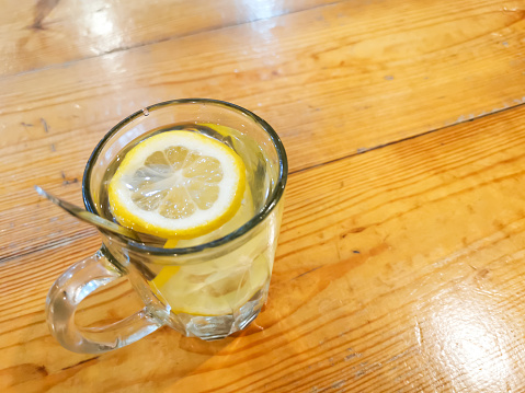 Glass cup of lemon drink with honey on wooden table.