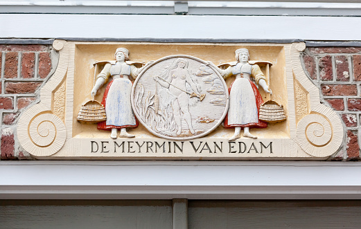 The fable of the Mermaid of Edam (De Meyrmin Van Edam), as depicted by this wall plaque in the town of Edam, Holland, dates back to 1403. In a heavy storm in 1403 waves destroyed the Zuiderzee protective dykes and water came gushing in to lake Purmermeer. and brought along with it a mermaid. When the storm calmed down, the dykes were quickly repaired and the Mermaid became trapped within lake Purmermeer. The Mermaid was often sighted by the two milkmaids (depicted on the plaque) on their way to milk their cows. As time passed the Mermaid and milkmaids became accustomed to seeing each other. Then one day, the mermaid came really close to their boat and the milkmaids saw an opportunity. They pulled the mermaid on board and took her back to Edam. The people from Edam then raised her as a human being. It was realised that she had a longing for the sea, and so she remained well guarded, so her escape would be difficult. Word spread of her existence and people came to visit Edam just so they could witness the so-called, Sea- Woman (Zeewijf). The powerful city of Haarlem made it known they wanted her to live in their city, so Edam presented the Mermaid to them as a gift. Haarlem gave her a home on the Grote Houtstraat and taught her to use the spinning wheel but she never adjusted to enable her speak freely with locals living nearby. During her lifetime she often went to church and had the habit of making a cross. The local people were convinced she had an affinity with the christian faith as she was often seen at church. At the end of her life she was buried as a christian.