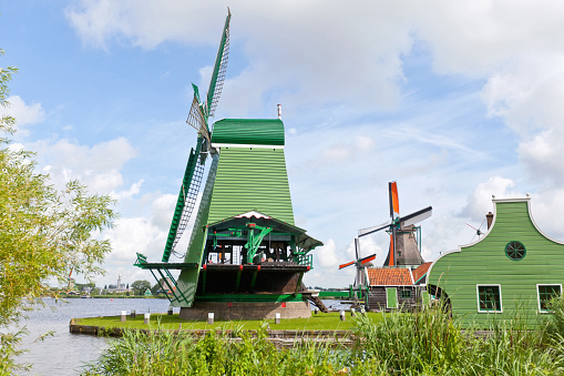Windmills at Zaanse Schans, Zaandam, Netherlands that stand on banks of the River ZaanSome of the windmills still use their wind-generated power to power sawmills and cut timber with the saws driven by wind power alone. Zaanse Schans is part of the European Route of Industrial Heritage: a tourist route of the most important industrial heritage sites in Europe.The windmill in the foreground is The Crowned Poelenburg (De Gekronde Poelenburg) with The Cat (De Kat) behind and the third windmill named, The Seeker (De Zoeker).